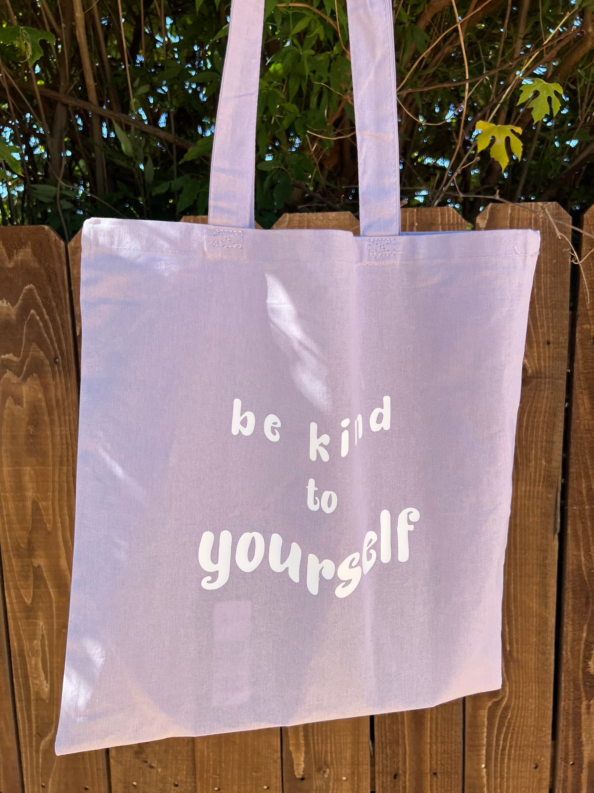lavender tote bag in front of brown fence and trees